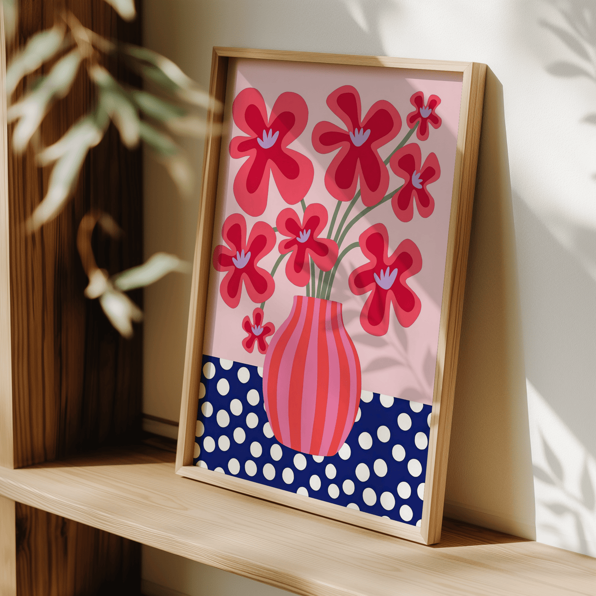 Framed close-up of colorful flower poster with red stylised flowers and a striped vase leaning on a wooden shelf