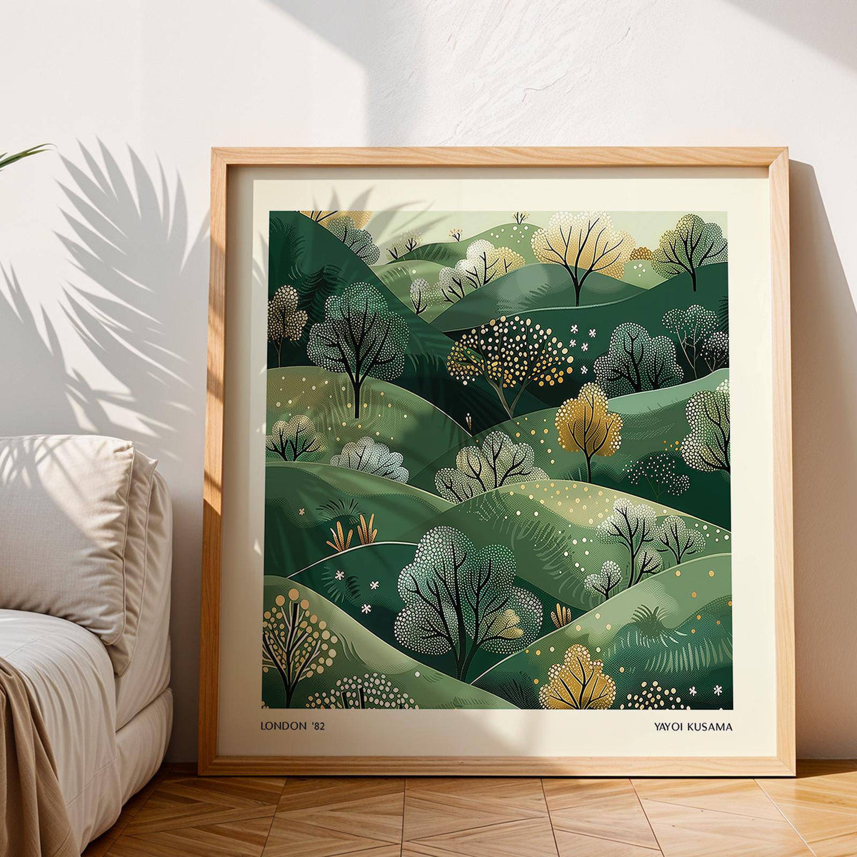 Framed large nature wall art with green hills and trees leaning on a wooden floor next to a sofa