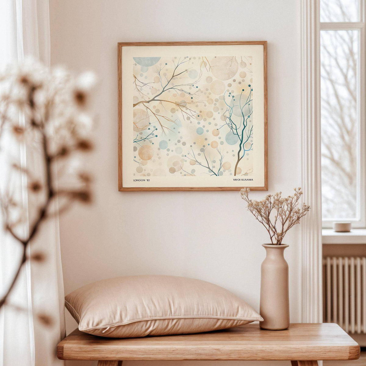Framed print of neutral artwork with delicate branches and berries in soft blue and beige above a wooden bench with a blush cushion