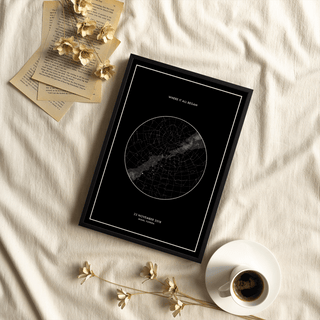 Framed Custom Star Map print with a black background and white typography on a fabric surface near a cup of coffee and dried flowers