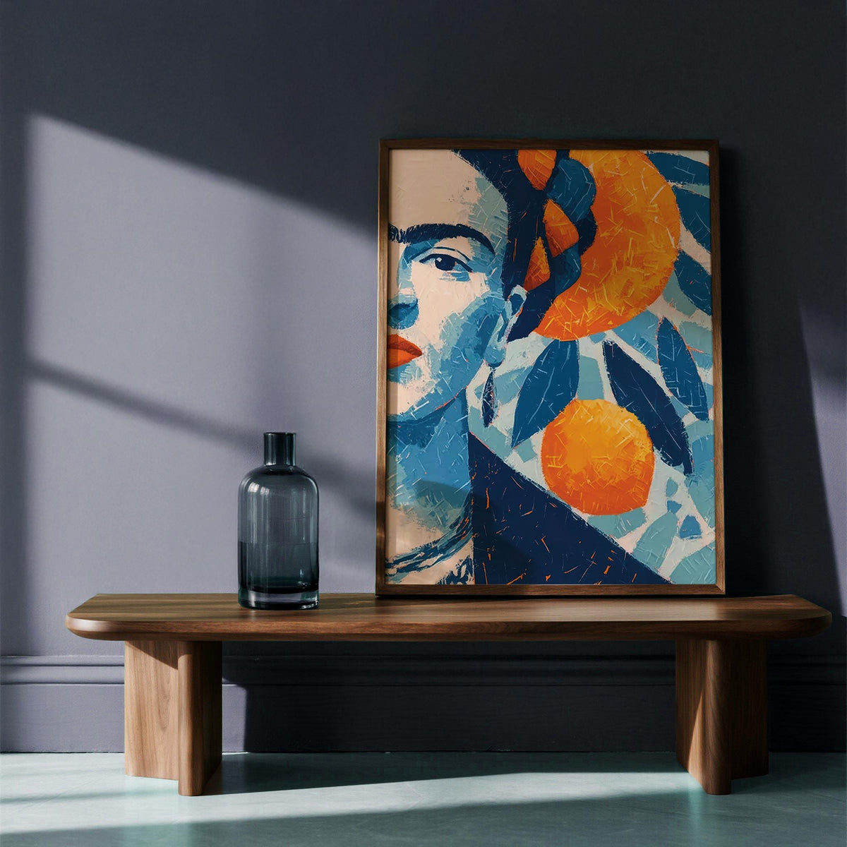 Print leaning on a wooden bench showing a female portrait with oranges and bold blues with an adjacent dark glass bottle