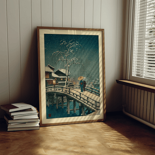 Print leaning on a floor of Hasui Kawase Snow Print showing a snowy bridge and two figures in traditional wear near window blinds
