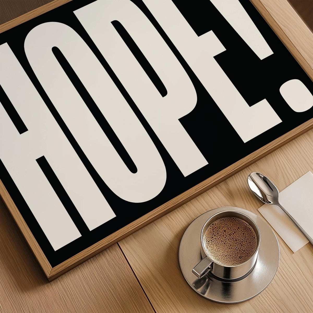 Framed close-up of HOPE! typography with black and white colours alongside a cup of coffee on a wooden surface