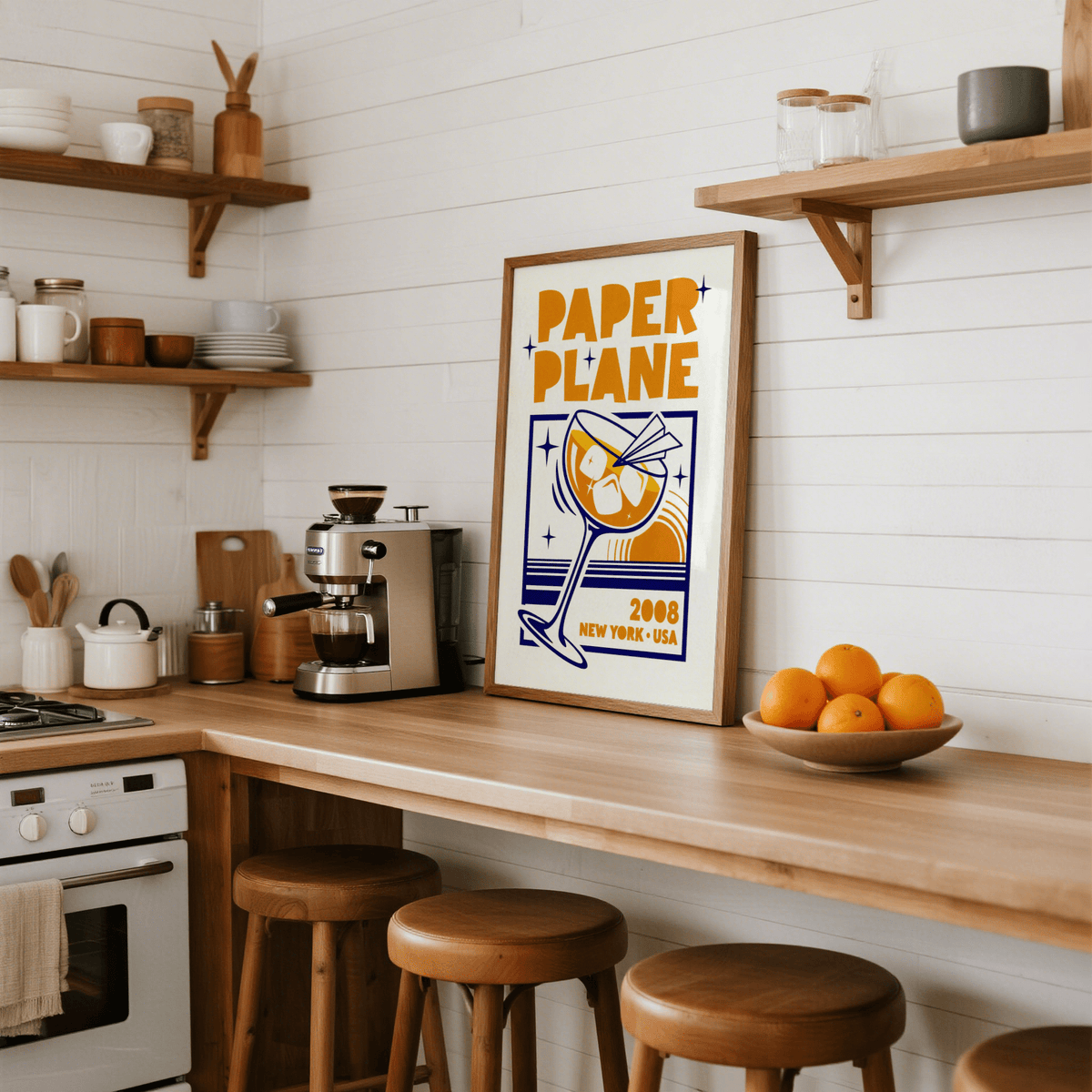 Print of Paper Plane Cocktail Poster leaning on a wooden kitchen countertop with a bowl of oranges