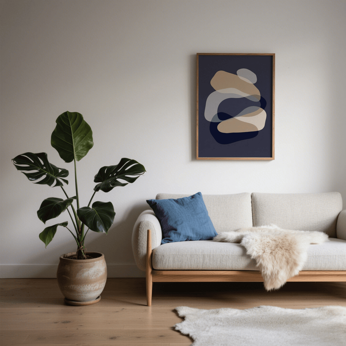 Abstract Art Shapes print with beige and grey shapes in a living room above a cream sofa with a blue cushion and plant
