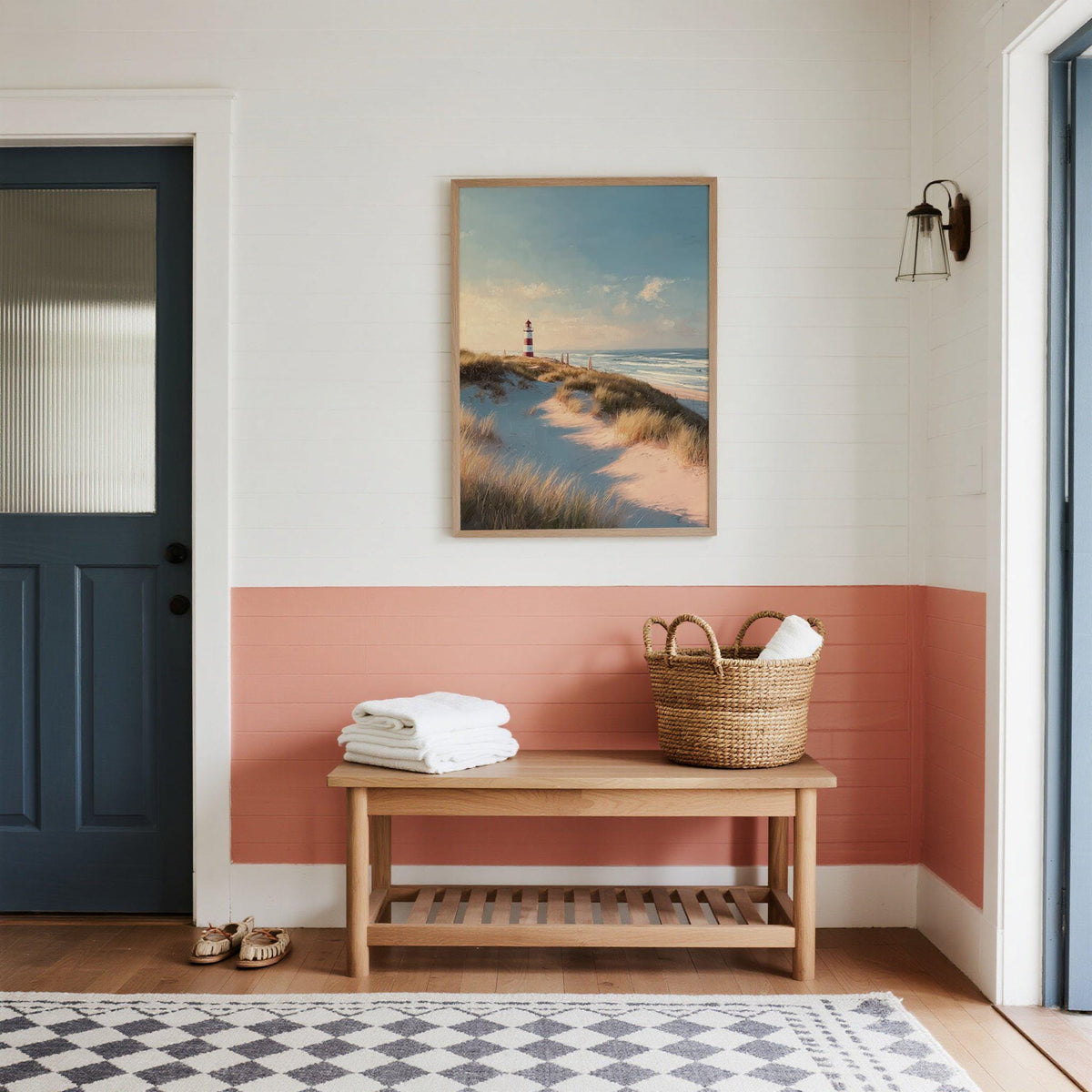Lighthouse wall art of a red and white striped lighthouse above grassy dunes in an entryway above bench with basket
