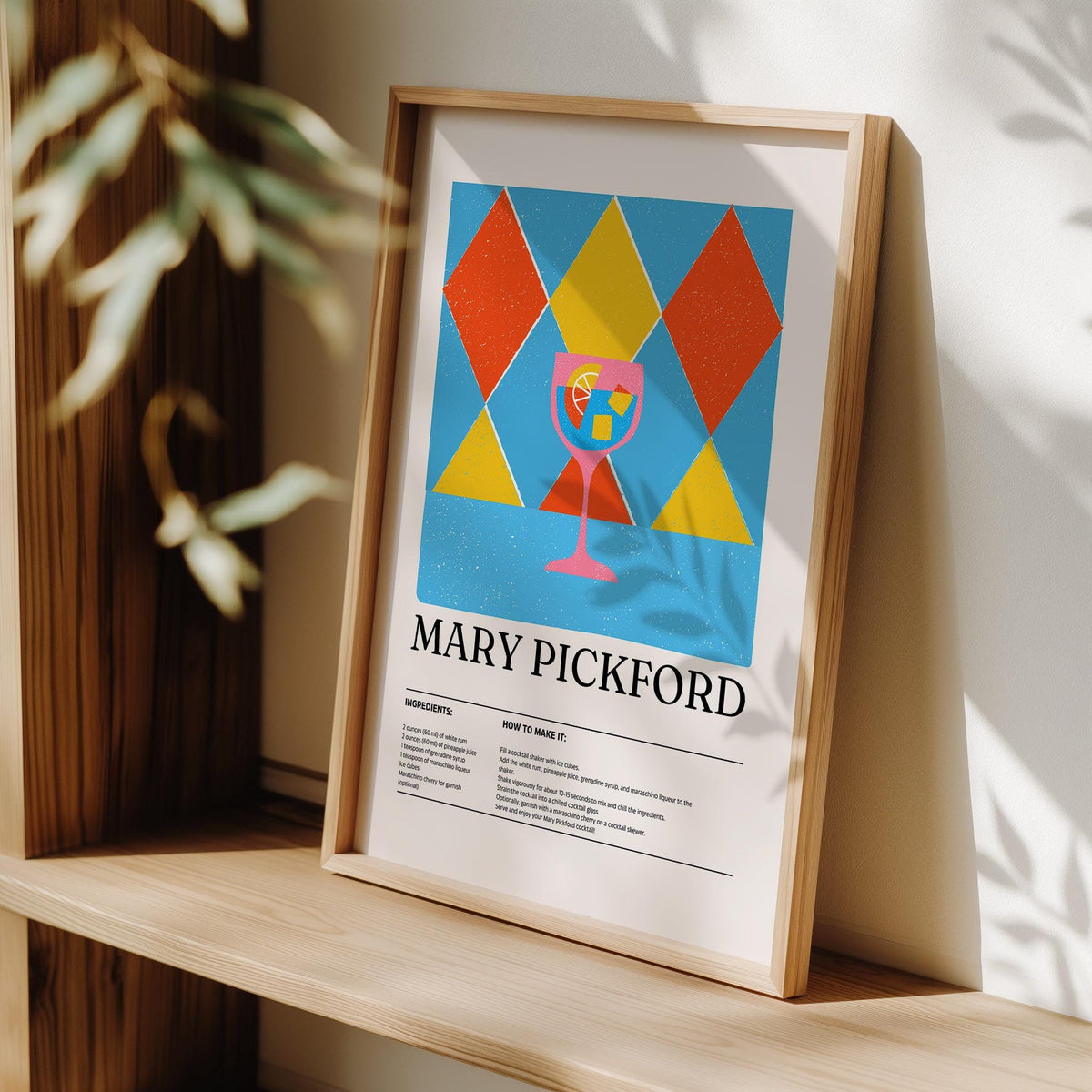 Framed print of Mary Pickford cocktail illustration in red yellow and blue leaning on a surface with a plant