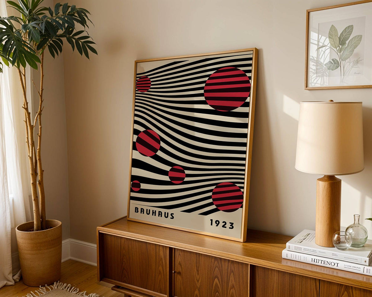Large Bauhaus wall art leaning on wooden sideboard with lamp and plant nearby