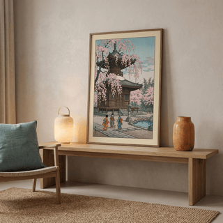 Framed Japanese Cherry Blossom Art Print leaning on a wooden bench with a lamp and ceramic vase nearby