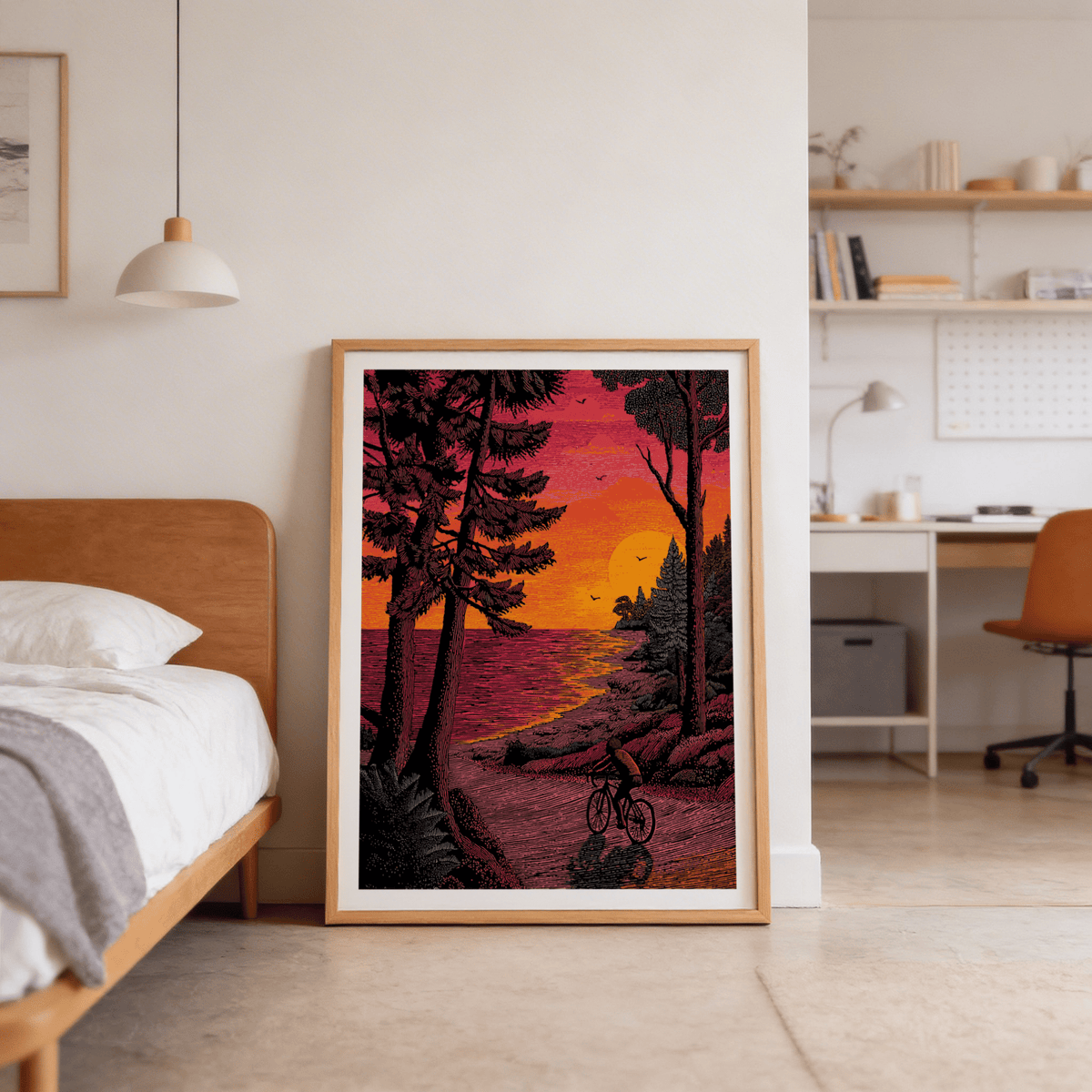 Print leaning on floor showing a cyclist at sunset with bright orange and red sky by a bed