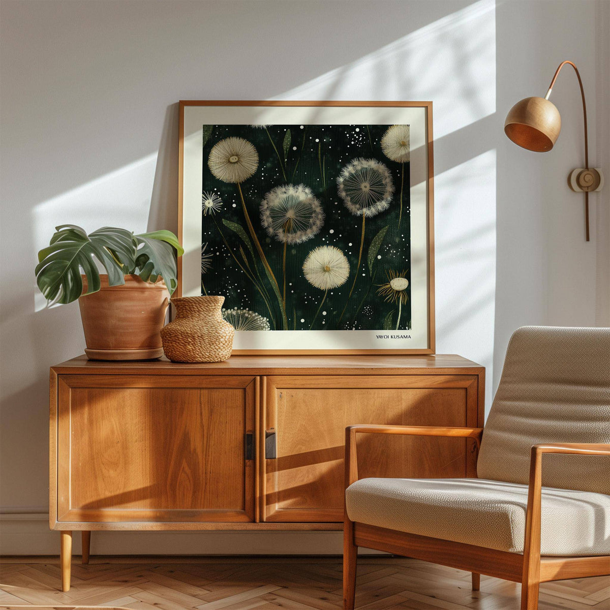 Square wall art of white dandelion seed heads on a dark background above a wooden sideboard with a plant and a wicker vase