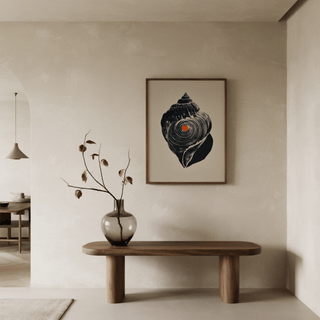 Shankha art print of a black sea shell with orange dot above a wooden table with a vase and dried flowers