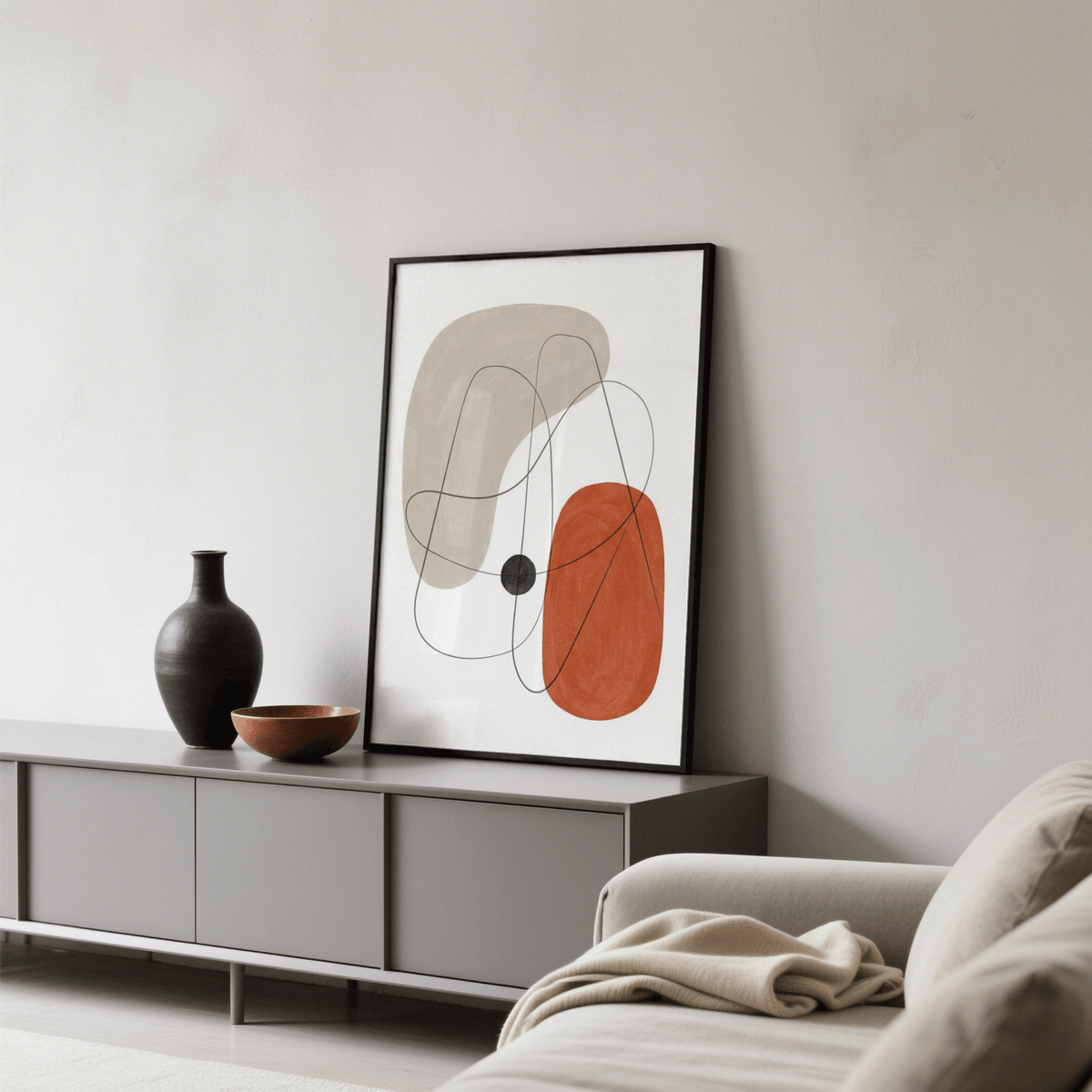 Abstract wall poster with red, beige and black organic shapes leaning on grey sideboard with a black vase