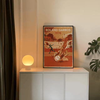 Vintage Tennis Art Print leaning on a white sideboard with a lit spherical lamp and a green plant