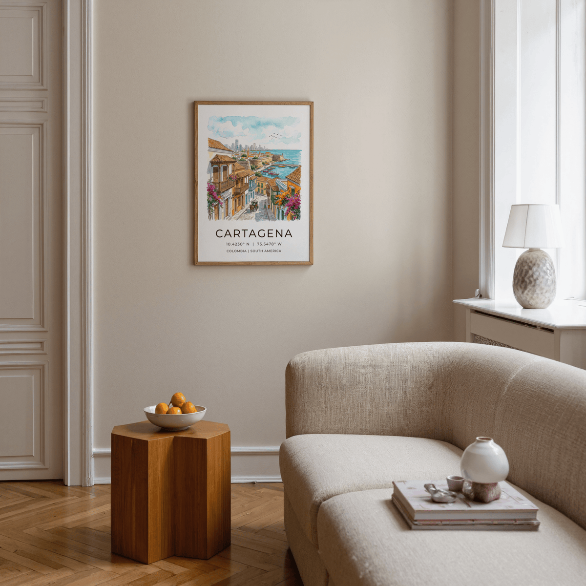 Cartagena Art Print framed on a beige wall above a wooden side table with a bowl in a living room