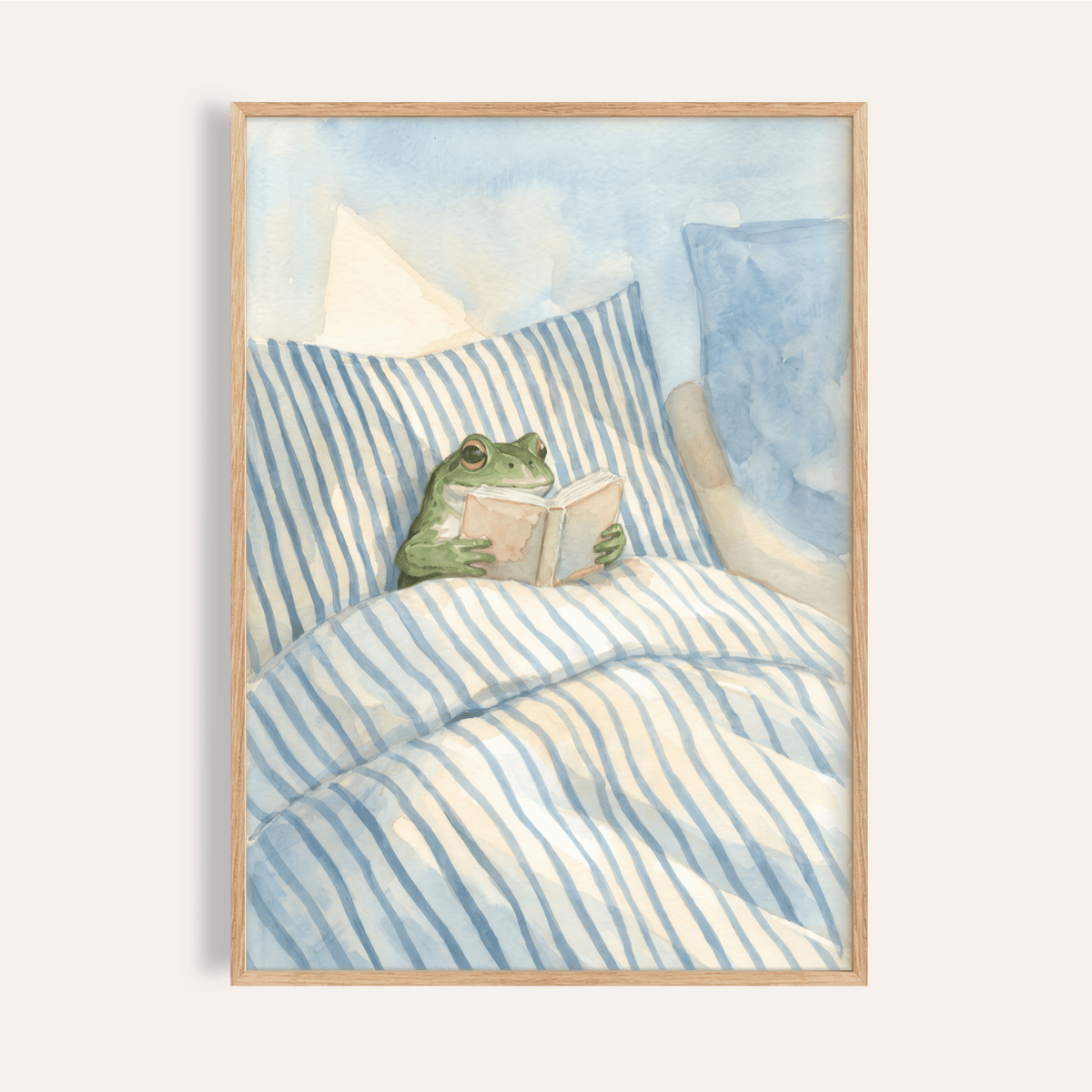 Framed print of a frog reading in bed with blue and white striped bedding in watercolour style
