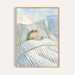 Framed print of a frog reading in bed with blue and white striped bedding in watercolour style