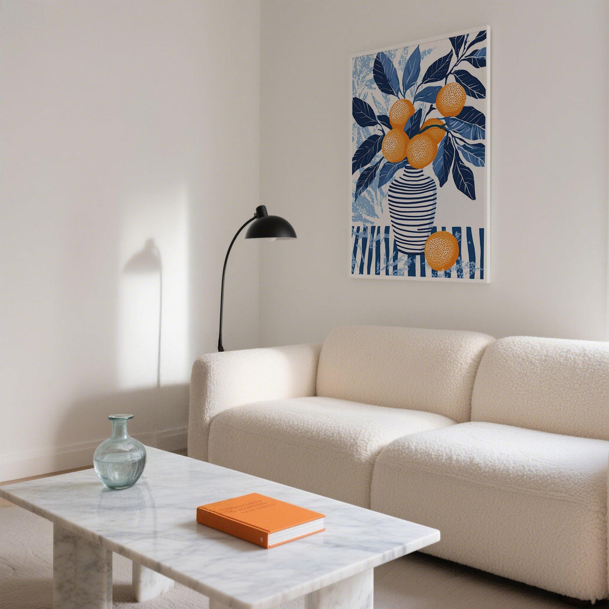 Print on a wall of oranges in a striped vase with blue leaves above a white sofa