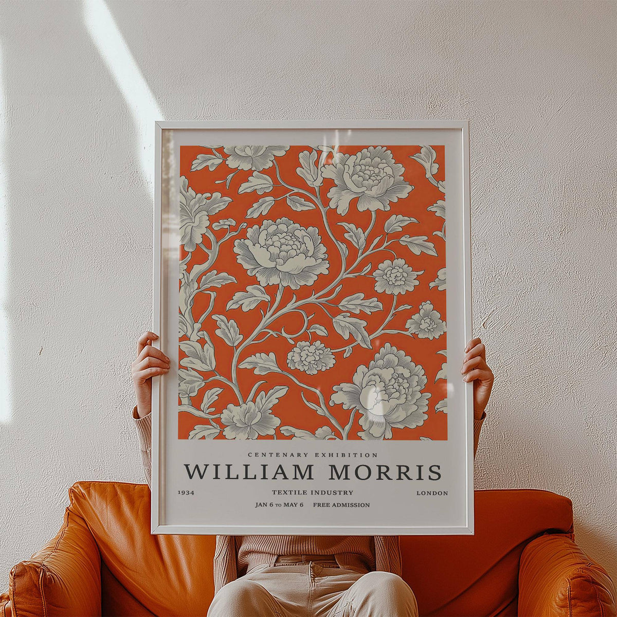 Framed print of Vintage Flower Art with white flowers on bright orange held against a plain wall above a brown leather sofa