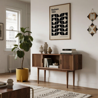 Print on a wall of a black and cream Bauhaus geometric pattern with a yellow plant pot beside a wooden sideboard