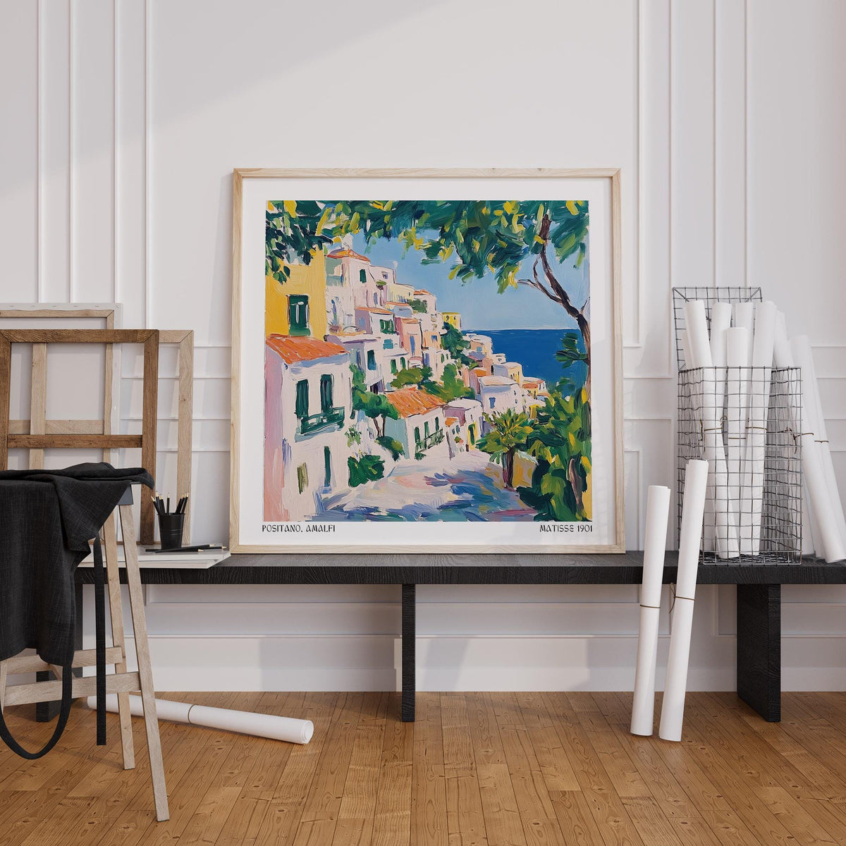 Print of Positano Art watercolour of an Italian coastal village leaning on a black shelf with rolled papers nearby