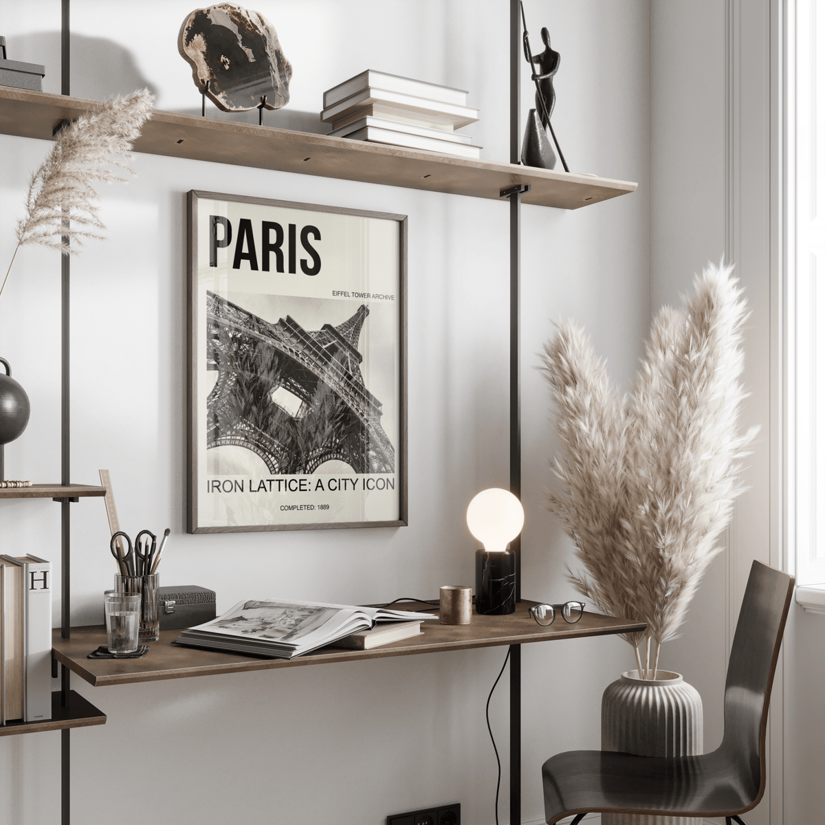 Paris Eiffel Tower print framed on wall above desk with books and pampas grass nearby