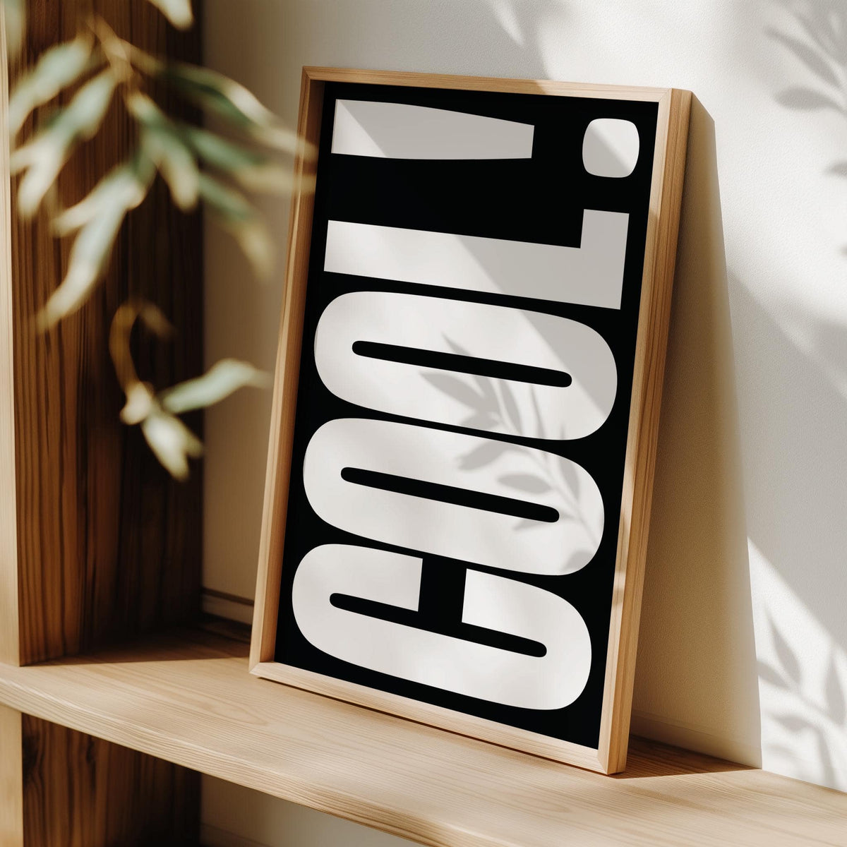 Framed print of Cool Typography Art leaning on a wooden shelf with light and plant shadows