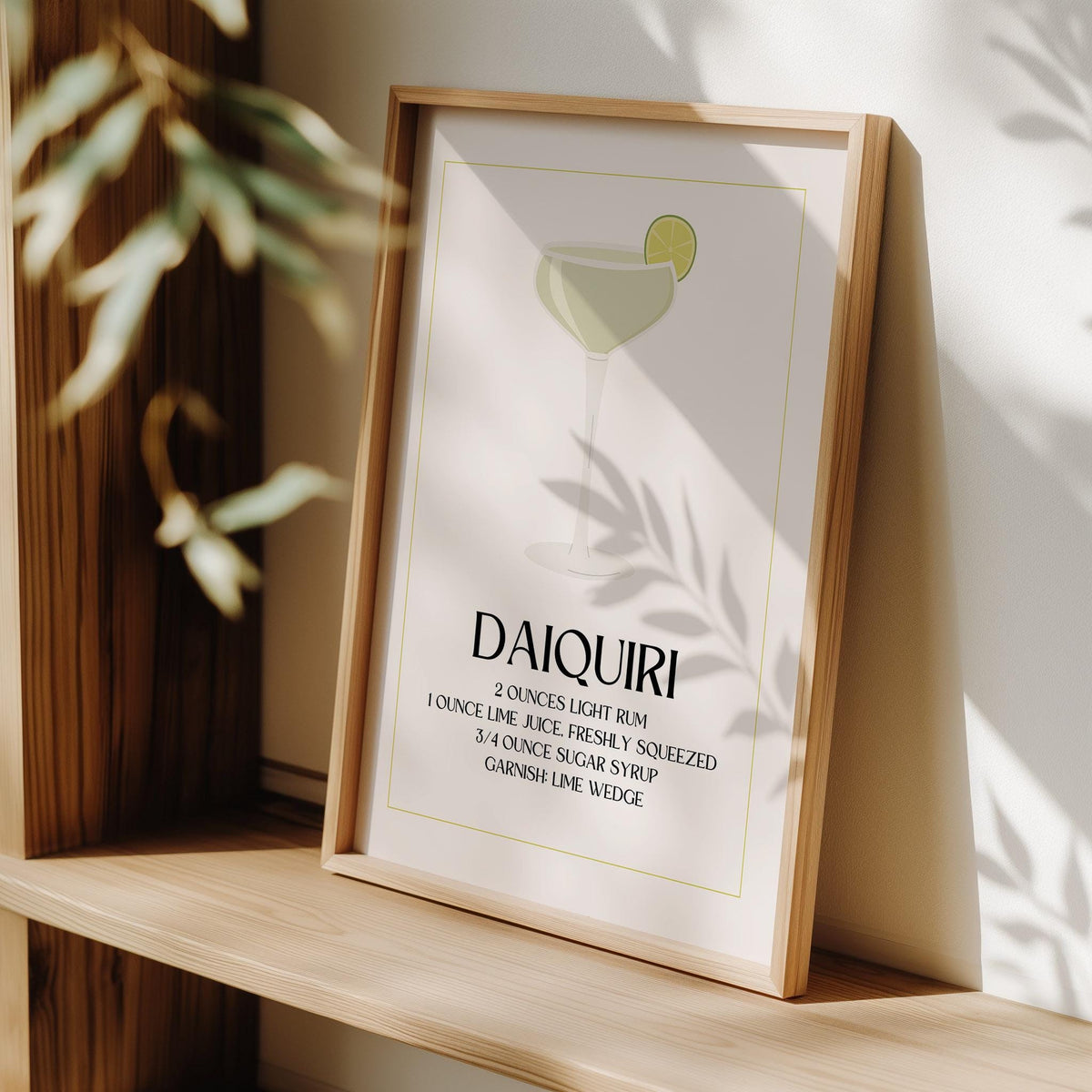 Minimalist daiquiri cocktail print with lime illustration leaning on a wooden surface with shadow of leaves