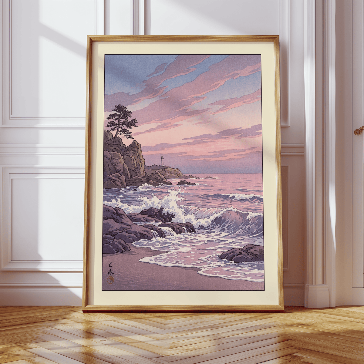 Print leaning on a wooden floor of rocky coastline at sunset with pink and purple tones near white wall