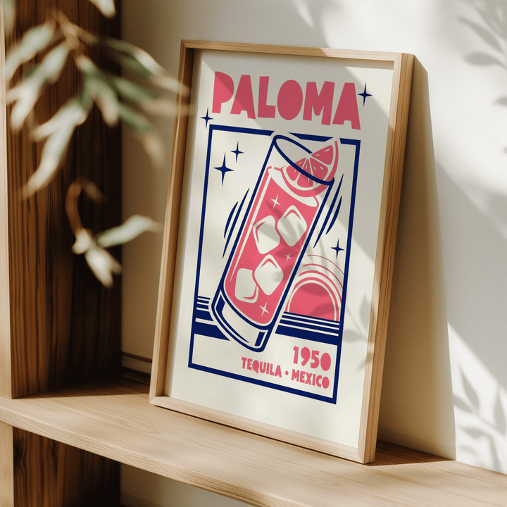 Framed Paloma Cocktail Print with mid-century style in pink and navy leaning on a wooden shelf