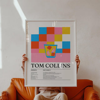 Framed print of a Tom Collins cocktail illustration with colourful blocks held by person on a brown sofa
