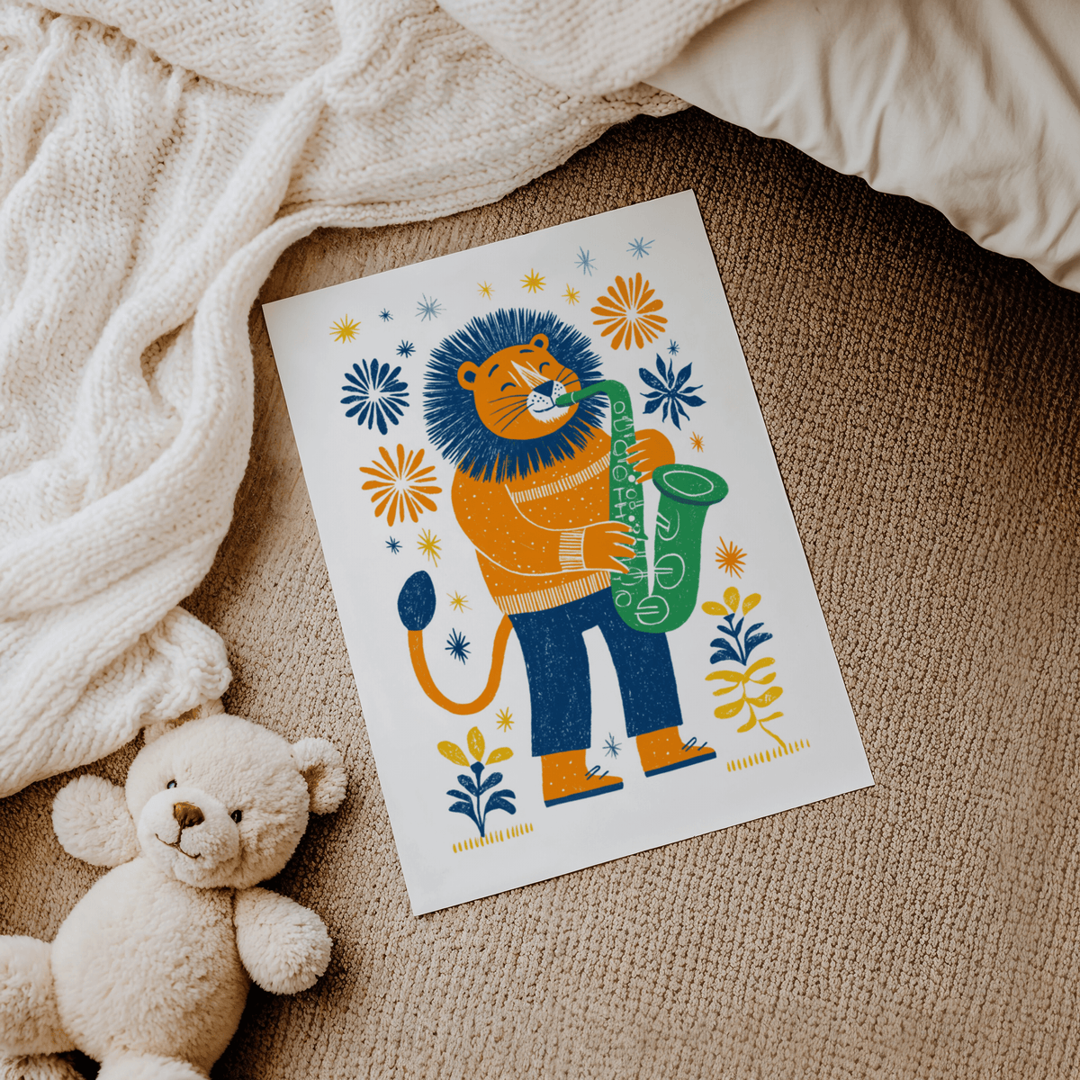 Saxophone Lion Art Print laid on a carpet next to a teddy bear with neutral-toned blanket