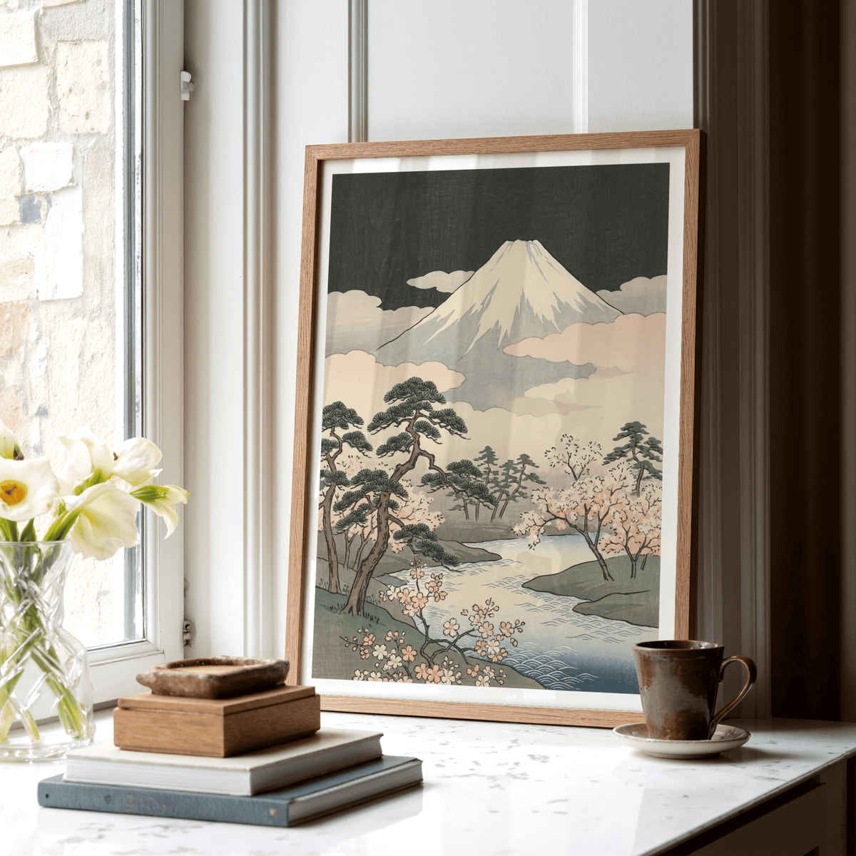 Print leaning on a surface with mountain and sakura trees in soft pink and grey tones with stacked books nearby