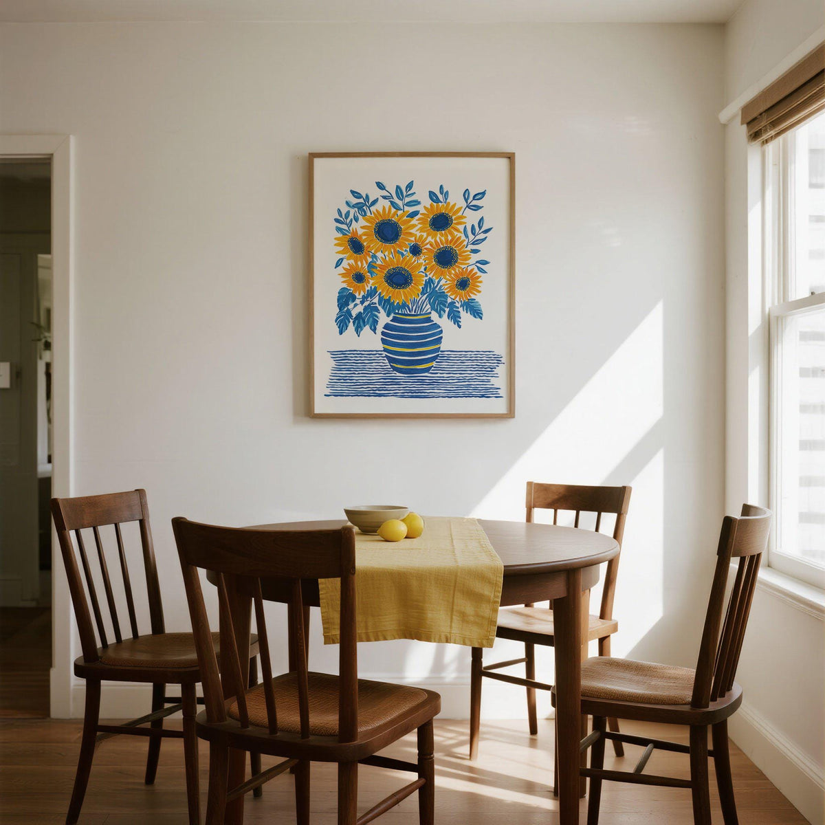 Print on a wall of a sunflower print with blue and yellow tones above a dining table with wooden chairs