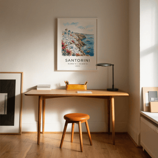 Santorini Art Print hanging above a wooden desk with a lamp and pencil holder in natural light