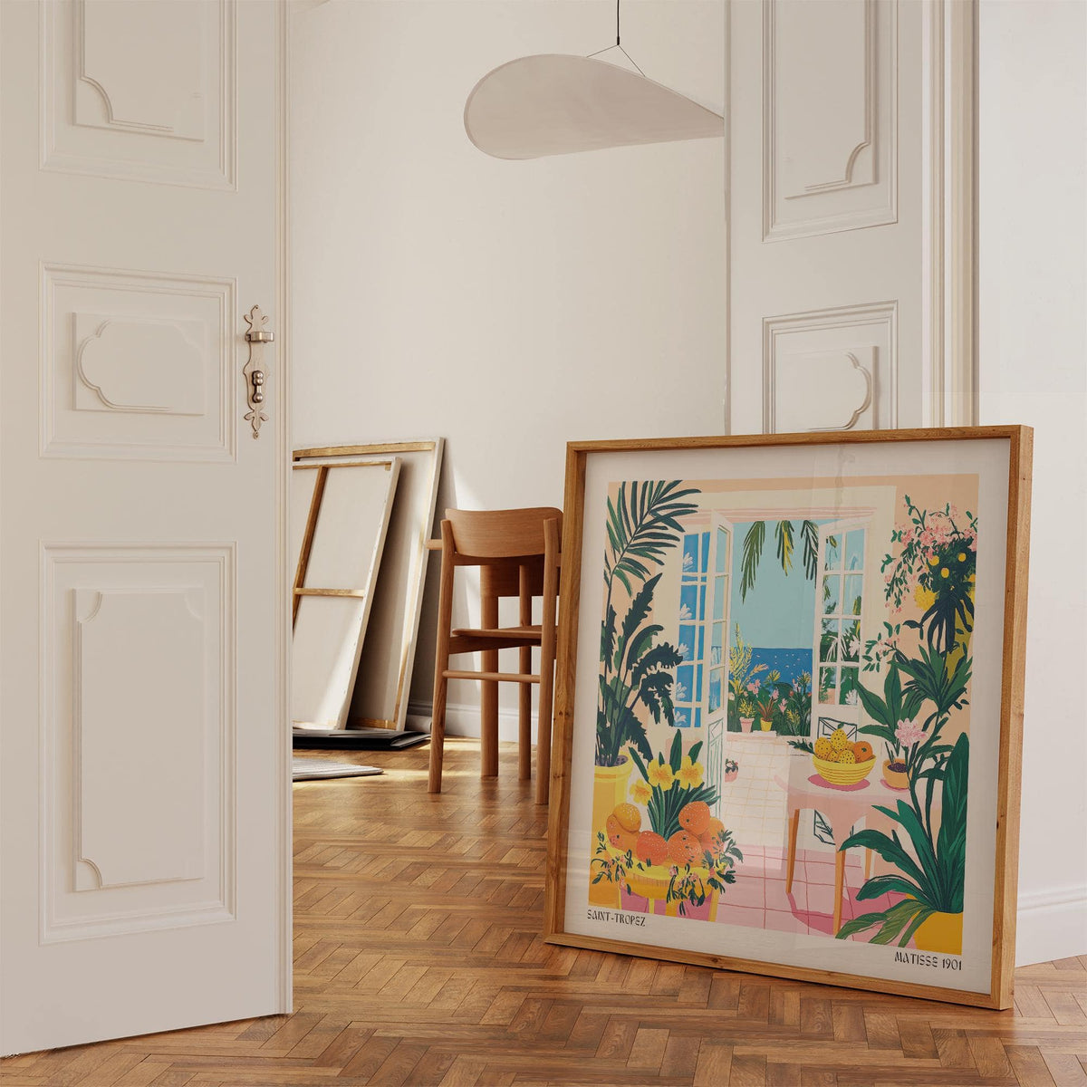 Print leaning on floor of coastal wall art with open doors and sea view surrounded by plants