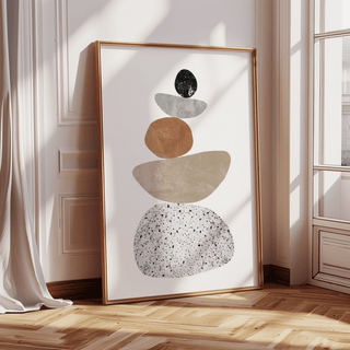 Print leaning on a floor showing minimalist abstract pebbles in neutral shades and black near curtains and a window