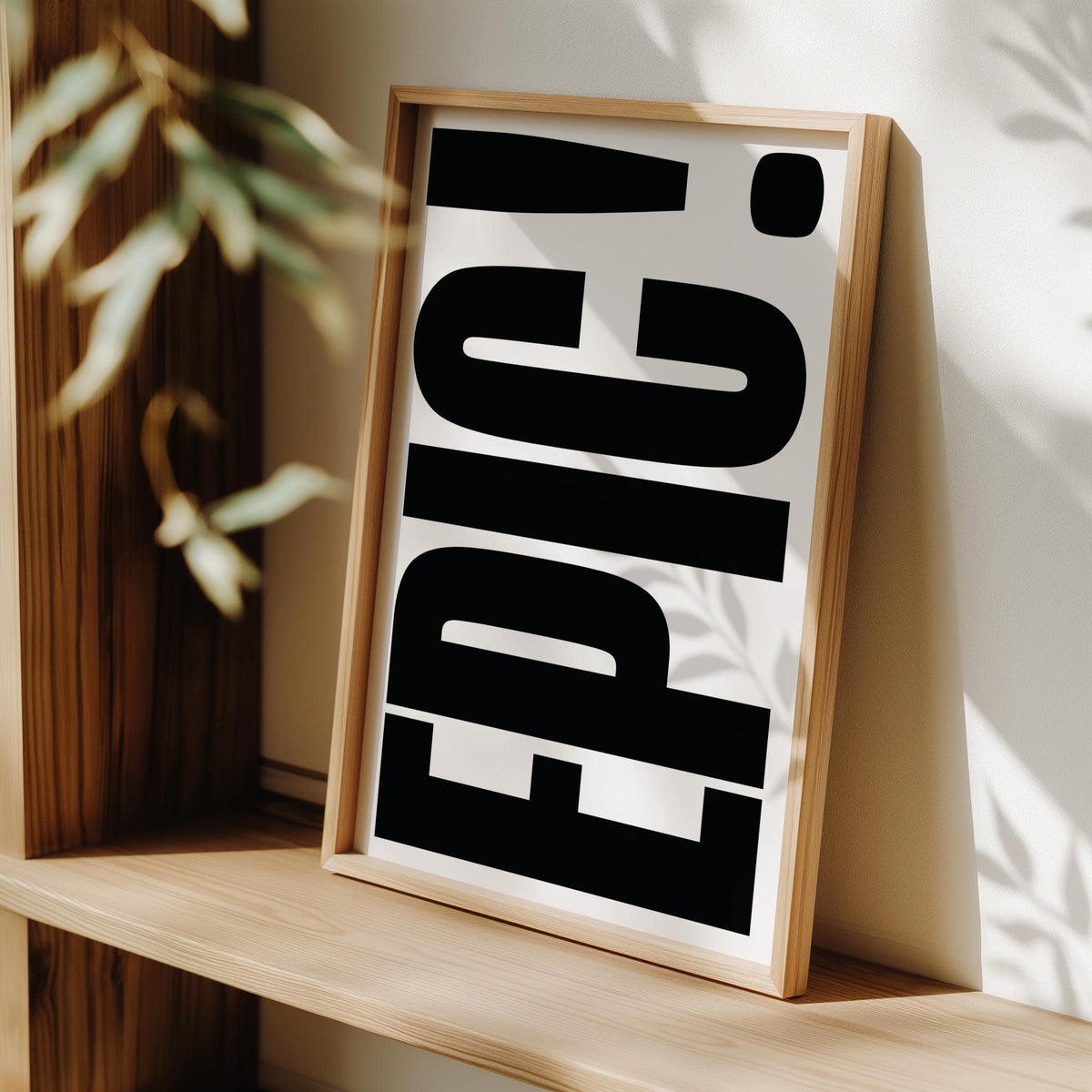 Framed print of Big Text Sign wall art with black EPIC typography leaning on a wood shelf