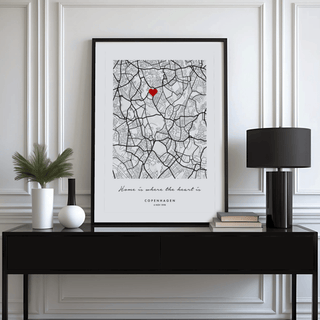 Framed Anniversary Map Print leaning on a black sideboard with a black lamp and green plant
