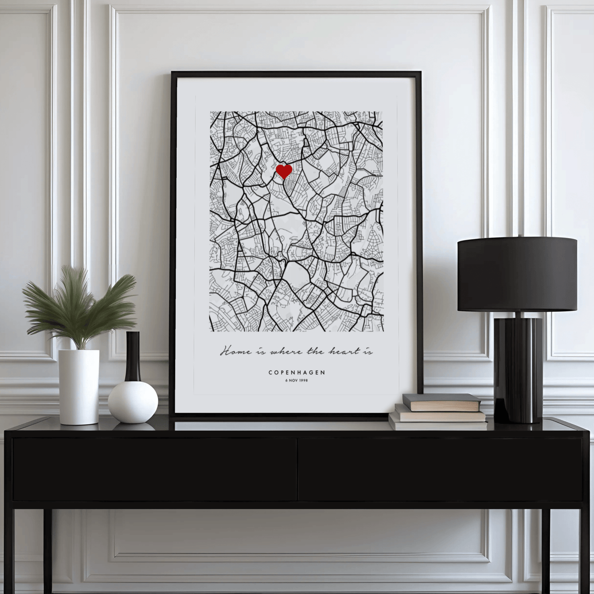 Framed Anniversary Map Print leaning on a black sideboard with a black lamp and green plant