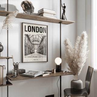 Framed Victorian London art print in black and white on a wall above a desk with books and a lamp
