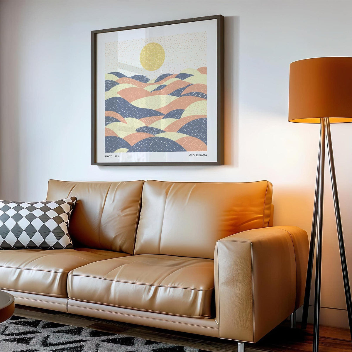 Print on a wall in a room showing abstract hills with sun in pastel shades above a tan leather sofa and beside a mustard floor lamp