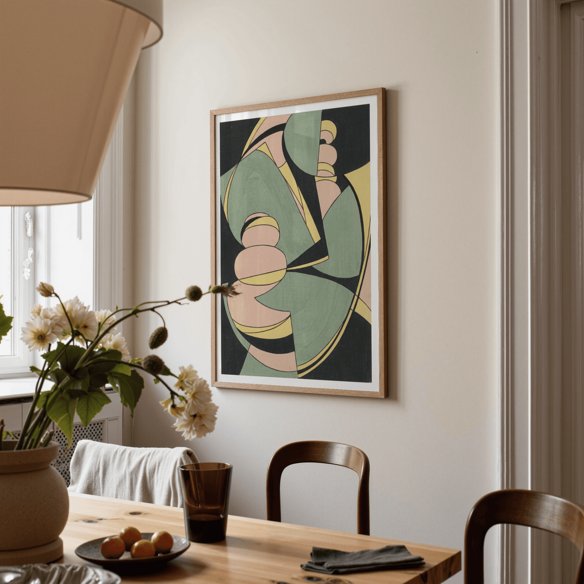 Abstract Geometric Art Print on a dining room wall with pastel shapes and a wooden frame above a wooden table with chairs