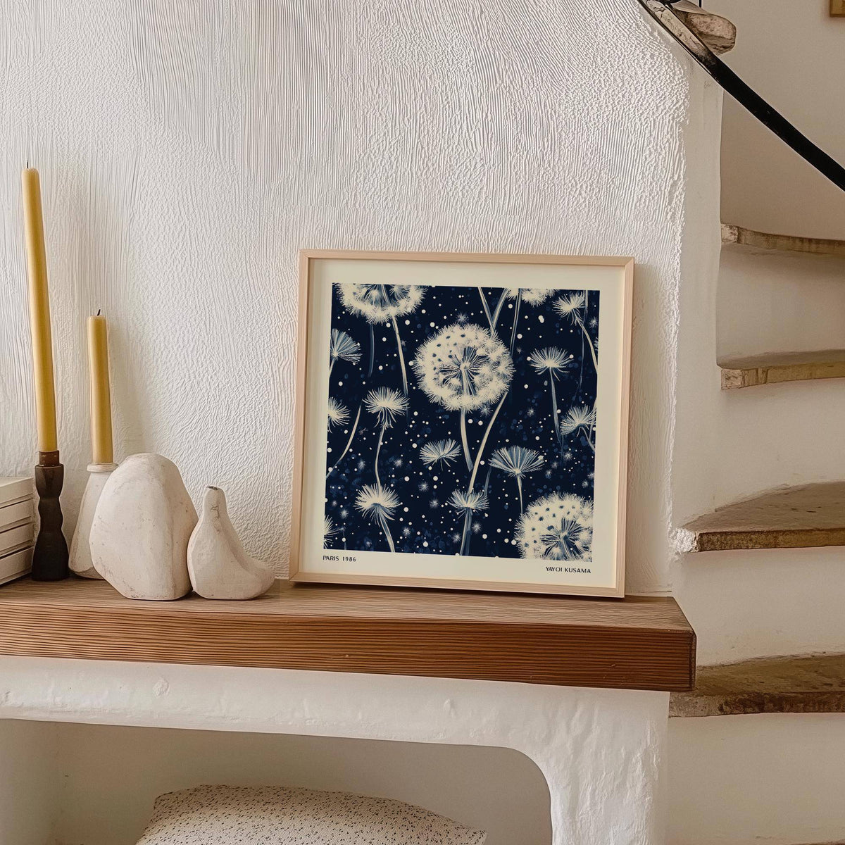 Print leaning on a shelf showing navy and white dandelion seed heads with candle holders nearby