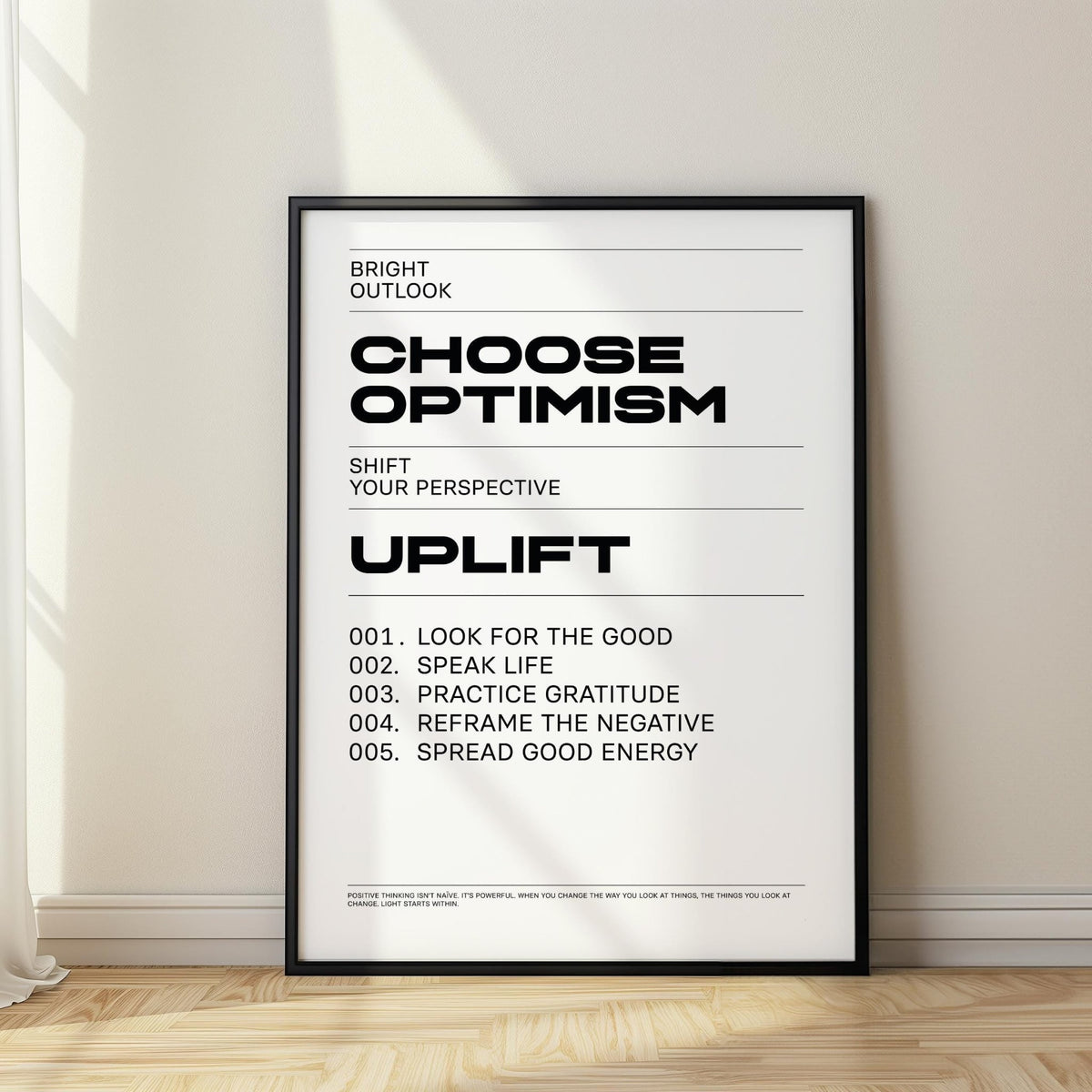 Uplifting wall art framed print with black and white minimalist motivational text leaning on a wooden floor near a curtain
