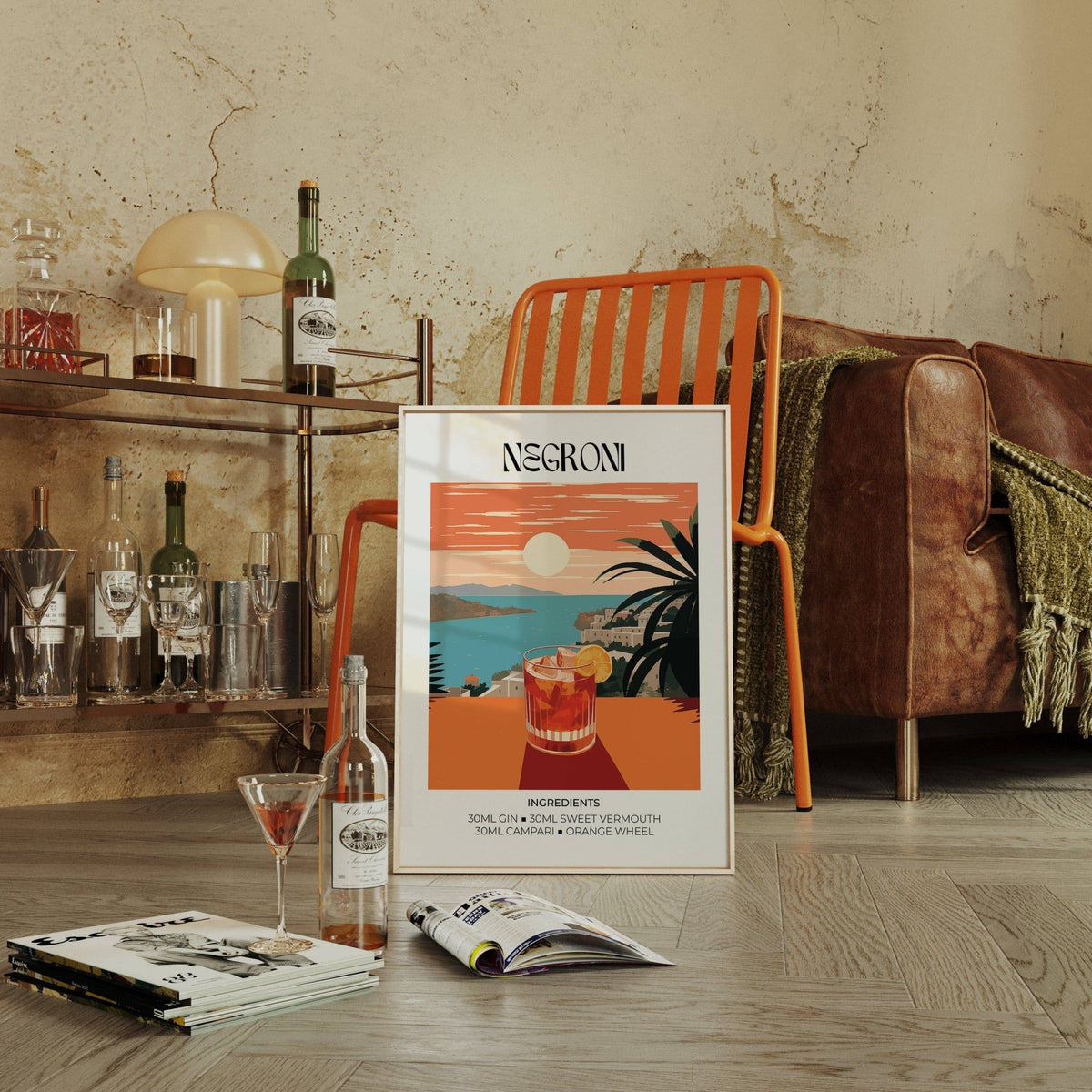 Print leaning on floor showing a Negroni cocktail glass with orange sunset and sea background with a modern chair nearby