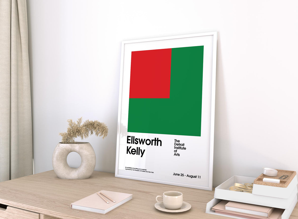 Print leaning on a shelf with red and green geometric shapes and black text with a cream vase nearby