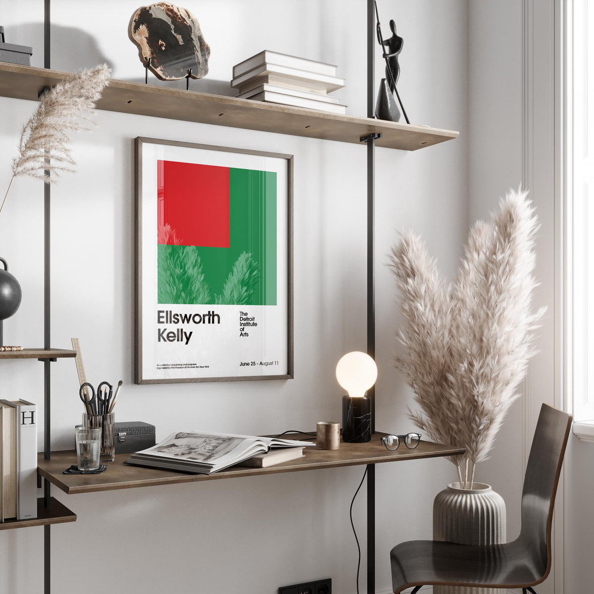 Office poster with red and green geometric shapes hanging above a wooden desk with a lamp and pampas grass