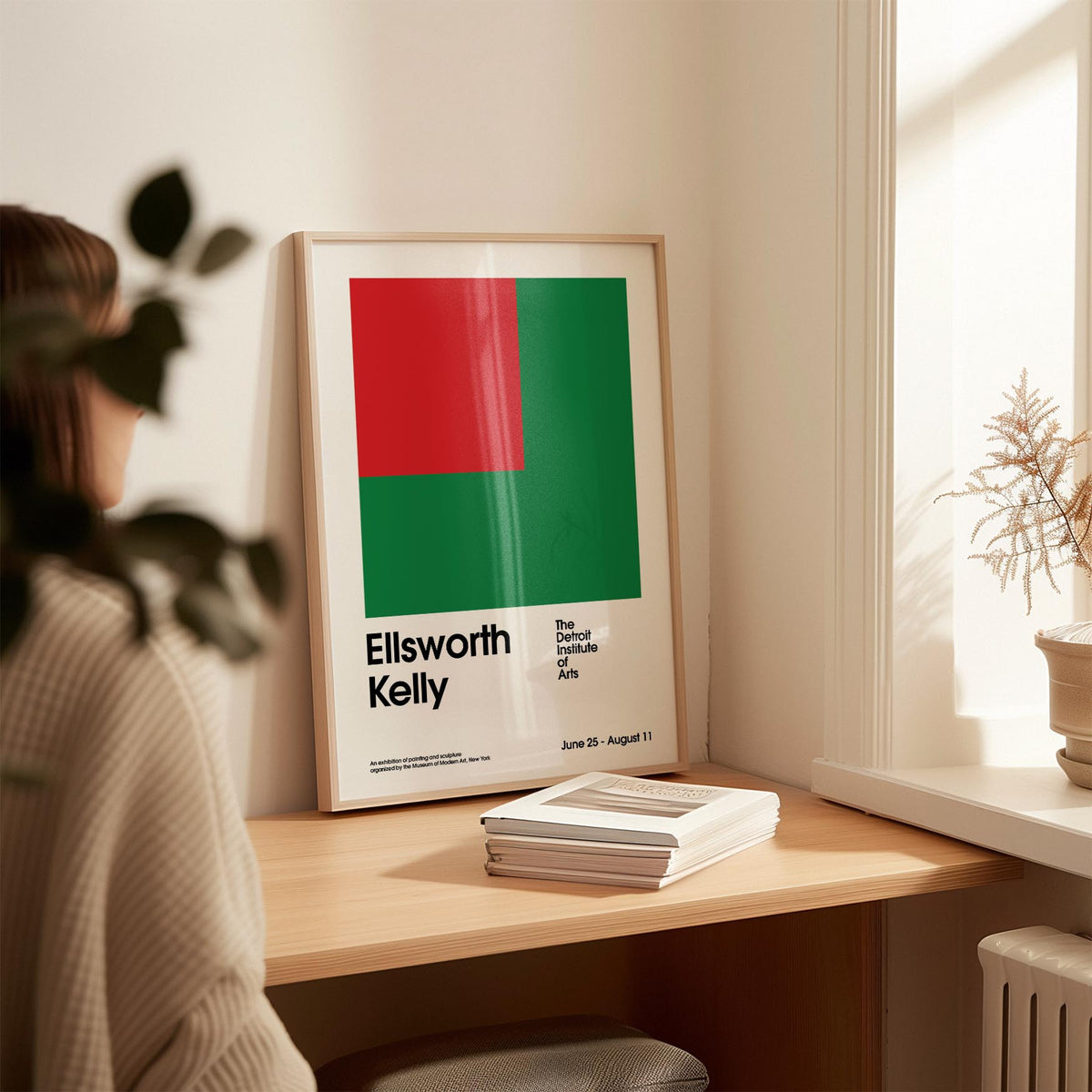 Office Poster leaning on a wooden desk with red and green geometric shapes and black text with a plant nearby