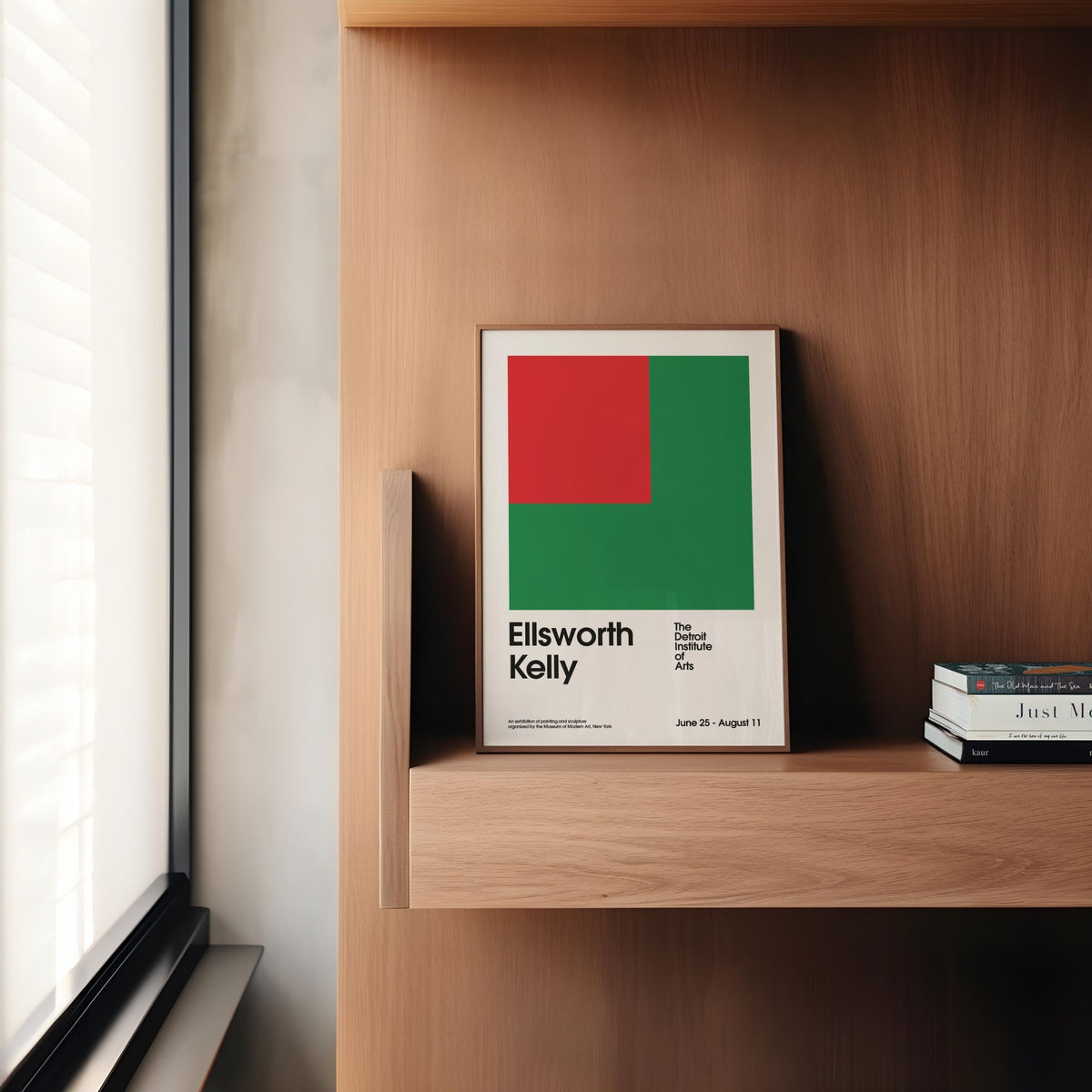 Office poster with red and green geometric shapes leaning on a wooden shelf beside stacked books